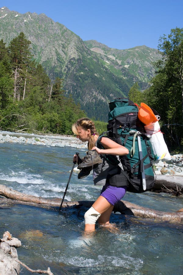 Backpacker girl moving across the mountain river. Backpacker girl moving across the mountain river