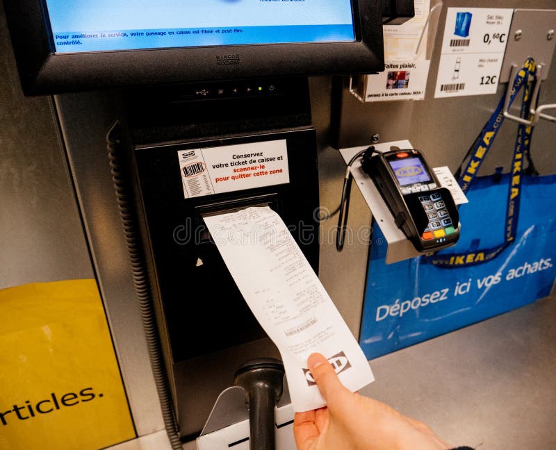 PARIS, FRANCE - SEP 2, 2017: Young woman taking receipt at the sef-service counter inthe IKEA furniture store scanning paying for products. PARIS, FRANCE - SEP 2, 2017: Young woman taking receipt at the sef-service counter inthe IKEA furniture store scanning paying for products