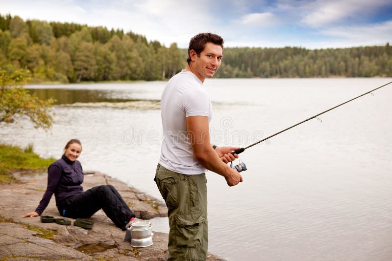 A man fishing on a lake with camping equipment and woman in background. A man fishing on a lake with camping equipment and woman in background