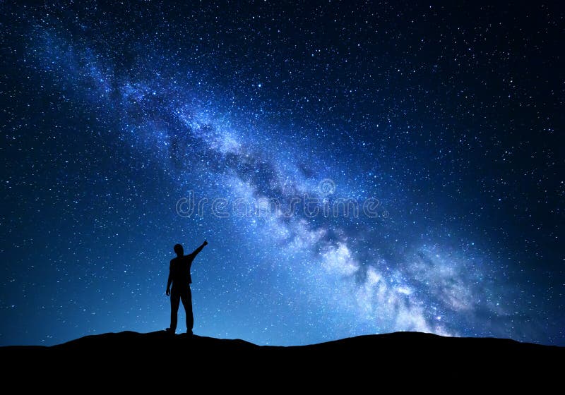 银河 指向在夜满天星斗的天空的一个常设人的剪影手指在山