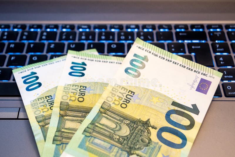 100 Euro Bills on Keyboard of a Laptop Computer - Home Office, Freelancing, Online Income Concept. 100 Euro Bills on Keyboard of a Laptop Computer - Home Office, Freelancing, Online Income Concept