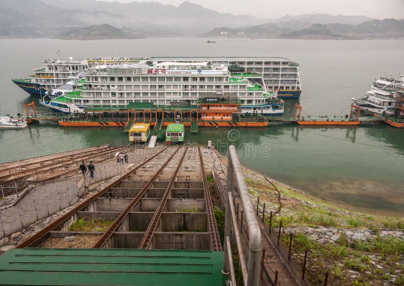 Three Gorges Dam, China - May 6, 2010: Yangtze River. 2 large passenger ships docked at Sandouping town on shore. Loaded with wagons on rails, steep descent. Landscape of river and hills on horizon. Three Gorges Dam, China - May 6, 2010: Yangtze River. 2 large passenger ships docked at Sandouping town on shore. Loaded with wagons on rails, steep descent. Landscape of river and hills on horizon