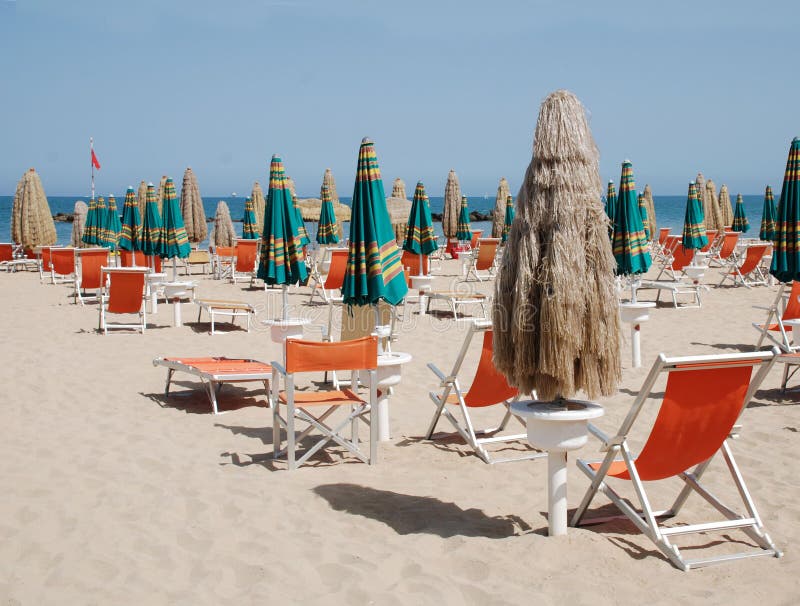 A closed brown beach umbrella and deckchairs on a beach on a sunny summers day. A closed brown beach umbrella and deckchairs on a beach on a sunny summers day