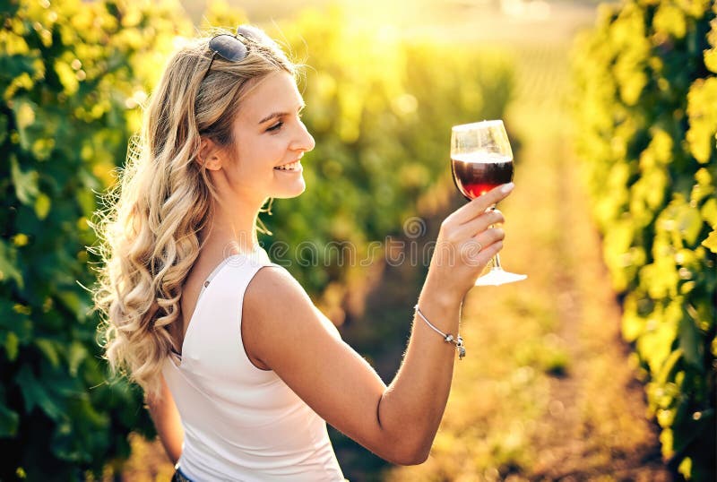 年轻的白人女性在阳光明媚的日子里在葡萄园里拿着一杯红酒，背面视图 - 酿酒、葡萄种植和葡萄酒 库存图片