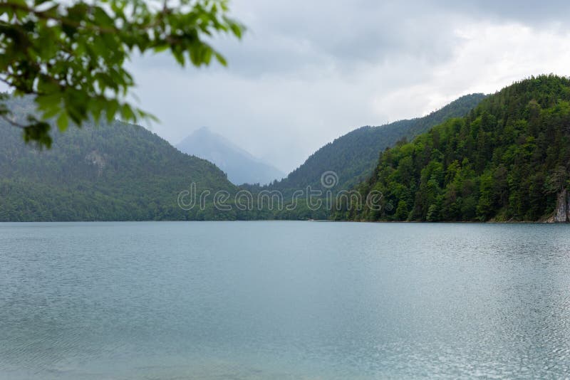 阿尔卑斯山围拢的Alpsee湖美好的哇明信片视图,巴伐利亚,德国 春天夏时 ?? 库存照片 阿尔卑斯山围拢的Alpsee湖美好的哇明信片视图,巴伐利亚,德国 春天夏时 ?? 库存照片
