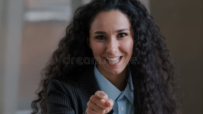 Arabian smiling curly woman employee business lady pointing index finger at camera emotionally speaking explaining corporate items hey you gesture support teaching giving advice agree opinion scolds. High quality photo. Arabian smiling curly woman employee business lady pointing index finger at camera emotionally speaking explaining corporate items hey you gesture support teaching giving advice agree opinion scolds. High quality photo