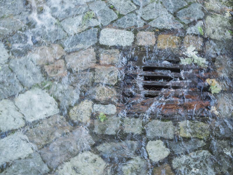 Elevated view on a rainwater runoff with inflowing water barrage between cobblestones in Berlin. Elevated view on a rainwater runoff with inflowing water barrage between cobblestones in Berlin.