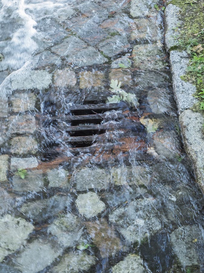 Elevated view on a rainwater runoff with inflowing water barrage between cobblestones in Berlin. Elevated view on a rainwater runoff with inflowing water barrage between cobblestones in Berlin.