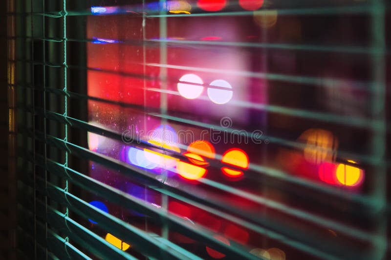 Bright colored spot lights shining through an open window blind at night. Bright colored spot lights shining through an open window blind at night.