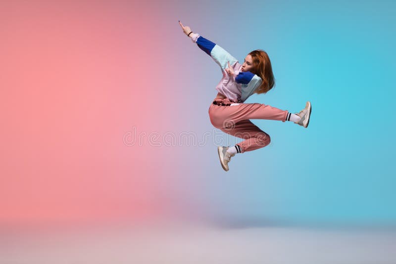 In jump. Beautiful girl dancing hip-hop in stylish clothes on colorful gradient background at dance hall in neon light. Youth culture, movement, style and fashion, action. Fashionable bright portrait. In jump. Beautiful girl dancing hip-hop in stylish clothes on colorful gradient background at dance hall in neon light. Youth culture, movement, style and fashion, action. Fashionable bright portrait.