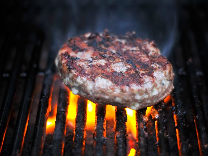 A juicy flame broiled bleu cheese burger cooking on the charcoal grill for dinner. The burger is smoking and has plenty of room for copy. A juicy flame broiled bleu cheese burger cooking on the charcoal grill for dinner. The burger is smoking and has plenty of room for copy.