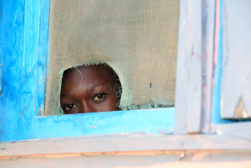 A kid looks with curiosity through window hole at visitors in Mankessim, a small junction town between Accra and Cape Coast in Southern Ghana (Western Africa). Nowadays, Mankessim attracts tourists by its largest-in-Ghana posuban, a sacred shrine that consists of three-storey construction with peculiar figures and symbols. Pusuban shrines are characteristic for central coastal Ghana and they are the work of asafo companies, military groups that are traditionally responsible for defence of towns in Akan societies. A kid looks with curiosity through window hole at visitors in Mankessim, a small junction town between Accra and Cape Coast in Southern Ghana (Western Africa). Nowadays, Mankessim attracts tourists by its largest-in-Ghana posuban, a sacred shrine that consists of three-storey construction with peculiar figures and symbols. Pusuban shrines are characteristic for central coastal Ghana and they are the work of asafo companies, military groups that are traditionally responsible for defence of towns in Akan societies.