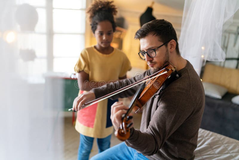 Music is so much fun. Young father teaching his little daughter to play violin and smiling. Parent child happiness concept. Music is so much fun. Young father teaching his little daughter to play violin and smiling. Parent child happiness concept.