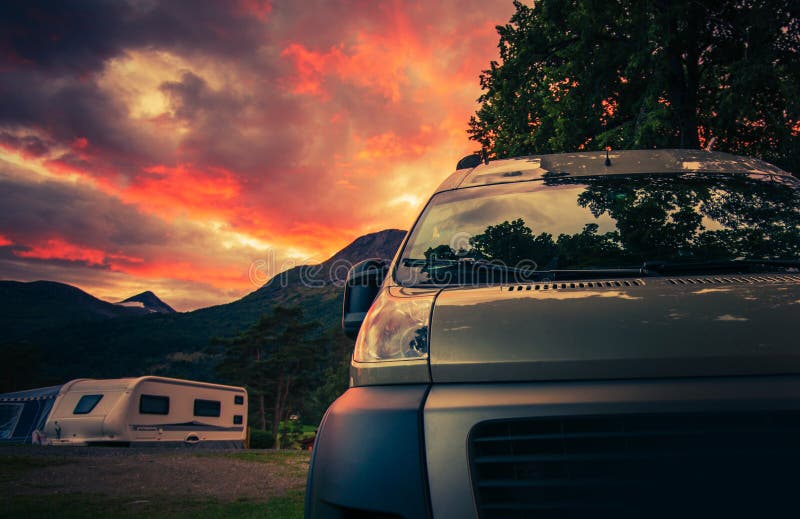 Scenic RV Park Camping During Beautiful Summer Sunset. Motorhome and Travel Trailers in the Background. Scenic RV Park Camping During Beautiful Summer Sunset. Motorhome and Travel Trailers in the Background.