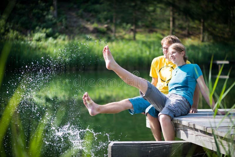 Young couple splashing water at lake sitting on wooden peer. Young couple splashing water at lake sitting on wooden peer