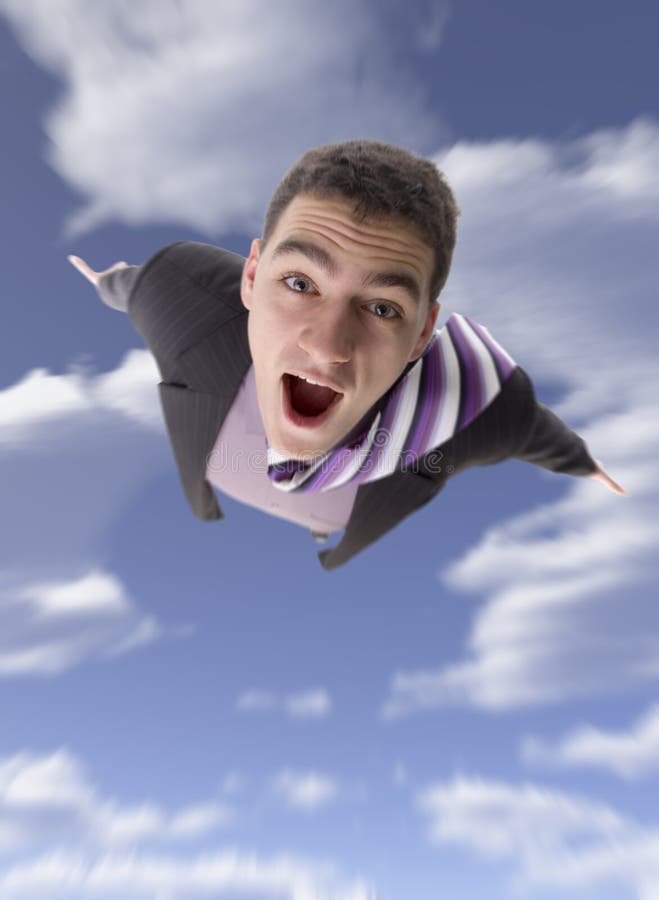 Young man appears to be flying, with mouth open in an amazed expression. Blue sky and clouds in the background. Young man appears to be flying, with mouth open in an amazed expression. Blue sky and clouds in the background.