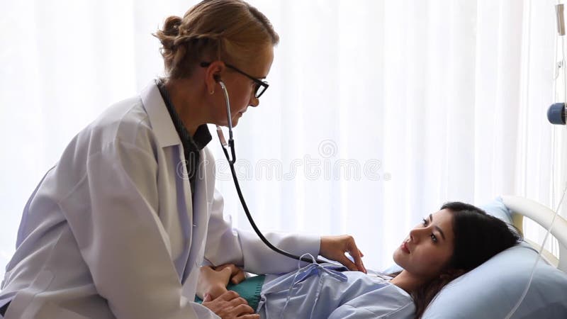 高级女医生在医院床上检查年轻病人心跳