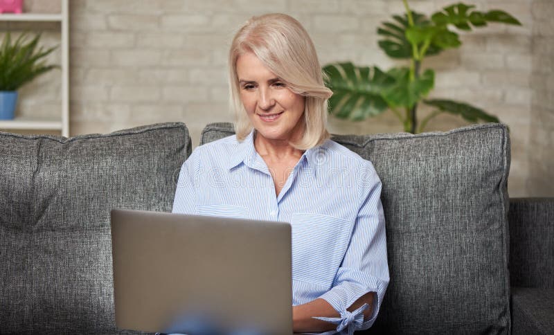 Senior woman is working on her laptop computer sitting on a sofa at home. Senior woman is working on her laptop computer sitting on a sofa at home