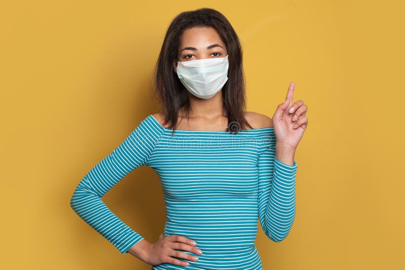 黄色背景上戴面罩的黑人妇女 流感疫情与病毒防护概念 库存照片