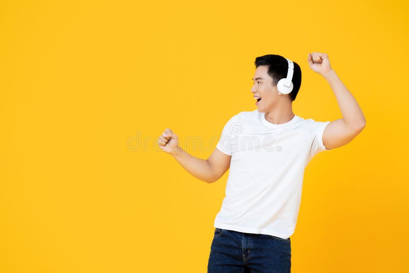 Young handsome Asian man wearing headphones listening to music and dancing on yellow background. Young handsome Asian man wearing headphones listening to music and dancing on yellow background