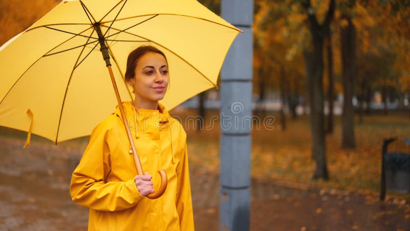 黄色雨伞慢动雨城公园的女孩. 侧视伞下躲在雨滴中的年轻女子. 行走