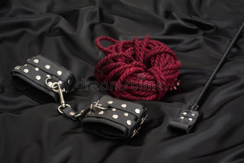 Leather handcuffs, shibari rope and stack on black background. Accessories for adult sexual game. BDSM outfit. Leather handcuffs, shibari rope and stack on black background. Accessories for adult sexual game. BDSM outfit