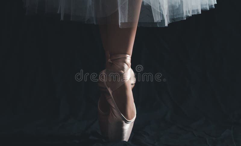 Close-up of dancing legs of ballerina wearing white pointe on a black background. Ballet dancer and practice concept background. Close-up of dancing legs of ballerina wearing white pointe on a black background. Ballet dancer and practice concept background