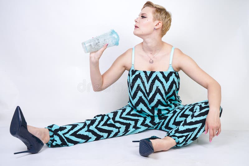 黑蓝色连衫裤的迷人的正大小年轻女人有杯的在白色背景的水在演播室 俏丽的白肤金发的女孩wearin 免版税库存图片 黑蓝色连衫裤的迷人的正大小年轻女人有杯的在白色背景的水在演播室 俏丽的白肤金发的女孩wearin 免版税库存图片