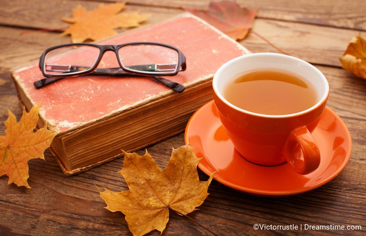 Autumn leaves, book and cup of tea on wooden table