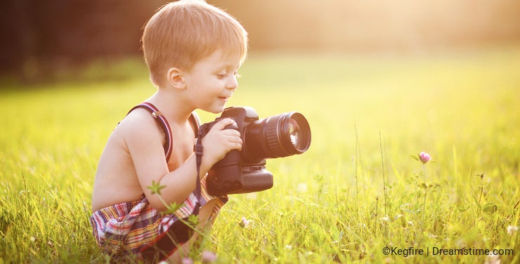 Smiling kid holding a DSLR camera in park