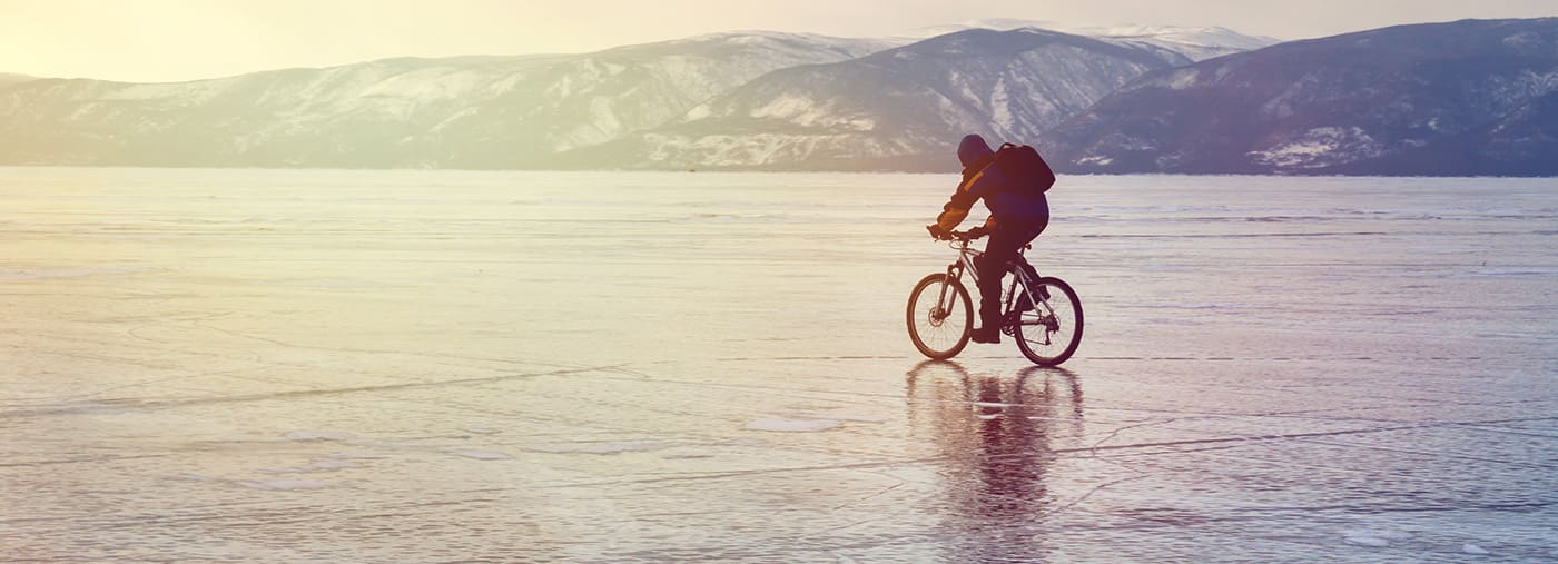 congele o viajante do motociclista com as trouxas na bicicleta no gelo lago baikal perspectiva céu por sol superfície esporte de