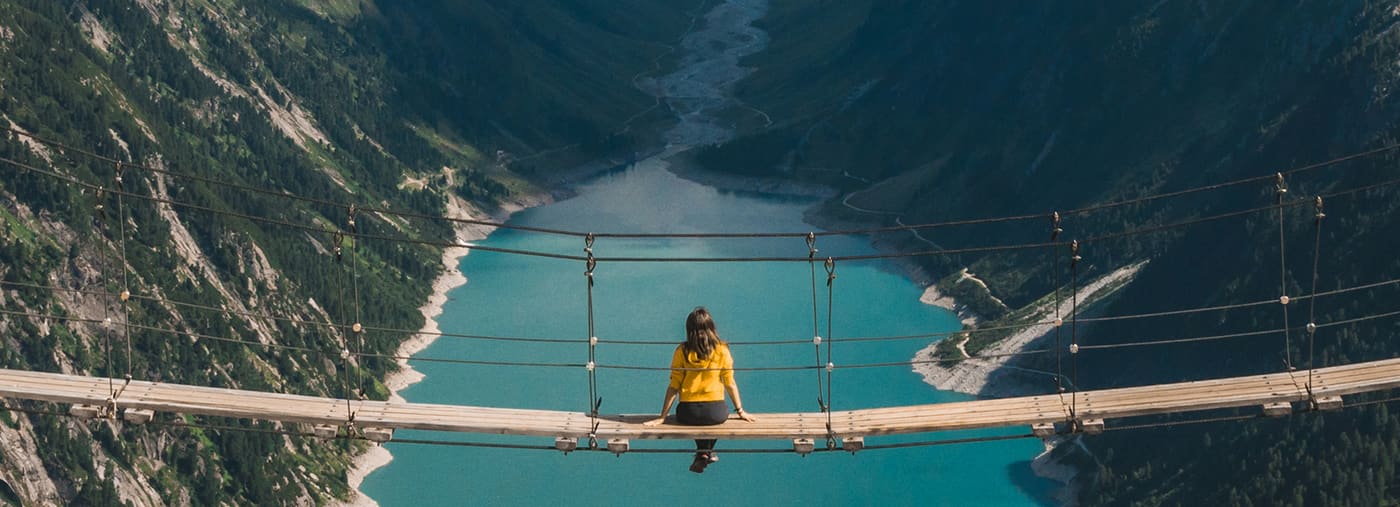 girl in blue tshirt and a yellow hat sitting on suspension bridge above the alps freedom adventure concept touristic activities