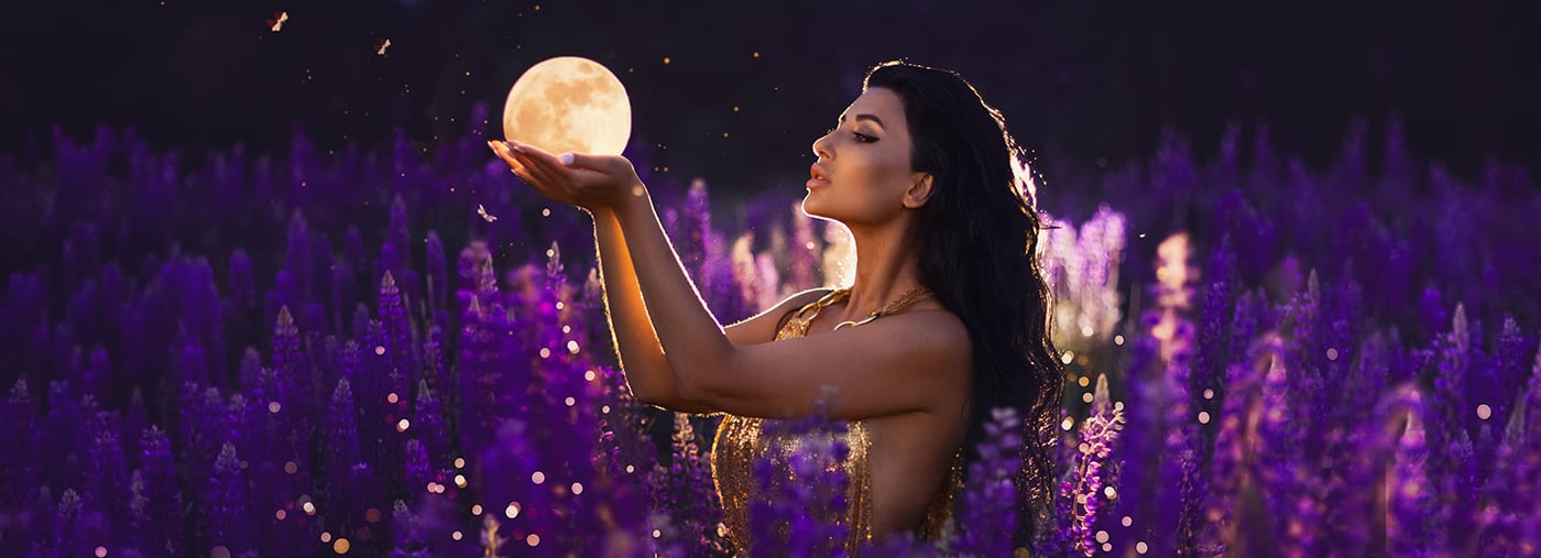 a brunette girl holding moon in her hands and standing among blooming purple lupine field golden dress with lights fireflies
