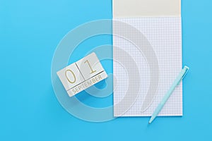 01 September. Wooden calendar on a blue background with an open notepad, top view