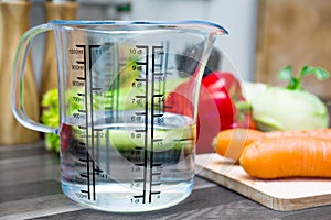 1/2 Liter / 500ml / 5dl Of Water In A Measuring Cup On A Kitchen Counter With Vegetables