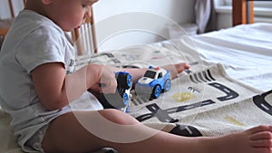 A 1 or 2 year old child plays with a screwdriver and toy police car in car repair sitting on bed at home