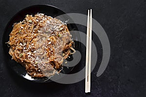 1 black plate brown Chinese cellophane rice noodles with shiitake mushrooms and peanut sauce, with sesame seeds on a dark