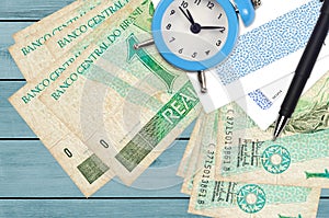 1 Brazilian real bills and alarm clock with pen and envelopes. Tax season concept, payment deadline for credit or loan. Financial