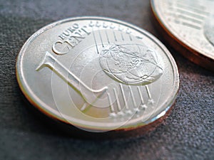 A 1 euro cent coin lies on a dark gray surface. Money close-up. Tinted illustration on economic or financial topic. The withdrawal