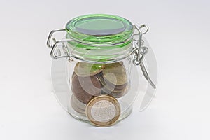 A 1 euro metal coin, a closed jar with small change on a white background, close-up, selective focus.Concept: financial savings, e
