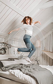 1 European   fun woman with red hair in jeans jumps on a bed smile,  in a bright room with a Christmas interior