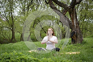 1  girl in a white top doing yoga in nature, on the grass among the trees