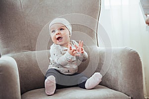 1 year girl wearing stylish clothes, sitting in a vintage chair in the room.