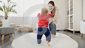 1 year old baby boy learning walking and making steps on carpet towards laughing mother. Baby development, family playing games,