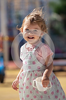 1 year old baby girl in the play garden with white cup. Portrait, macro. Outside children park, summer