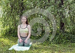 1 young woman in sportswear sitting on a green yoga Mat among the trees in the garden in the spring