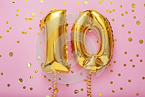 10 air balloon numbers on pink background. 10 k gold foil balloons with confetti. Birthday party flat lay with copy space