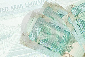 10 UAE dirhams bills lies in stack on background of big semi-transparent banknote. Abstract presentation of national currency