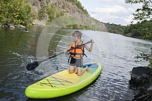 A 10-year-old boy rides a SUP board alone on a mountain lake, river, canyon.