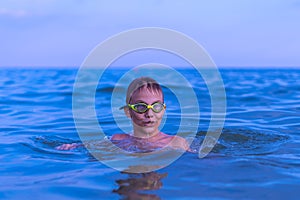 A 10-year-old boy swims in the sea at dawn with glasses for swimming